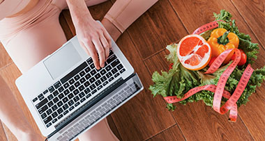 person using a laptop with fresh vegetables and measuring tape indicating healthy meal planning for 10 lifestyle tips