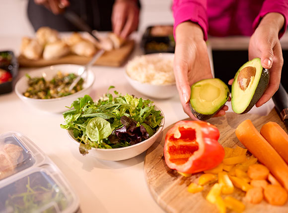 hands holding avocado with sliced vegetables and bowls of salad and rice on the table in a healthy meal preparation scene emphasizing balanced nutrition and nine essential nutrients